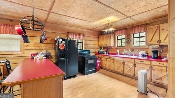 kitchen featuring pendant lighting, wood walls, light hardwood / wood-style flooring, and black appliances