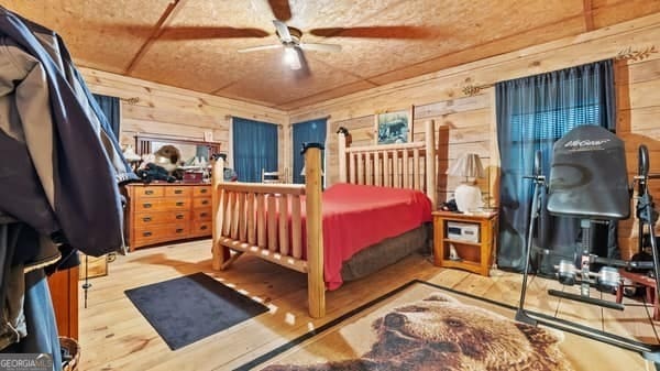 bedroom with wooden walls, ceiling fan, and wood-type flooring