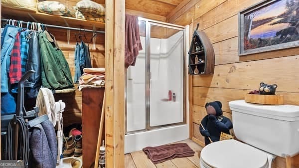 bathroom with hardwood / wood-style flooring, toilet, a shower with shower door, and wooden walls