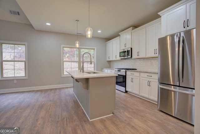 kitchen featuring white cabinets, a center island with sink, stainless steel appliances, and a healthy amount of sunlight