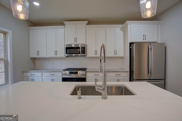 kitchen with white cabinetry, appliances with stainless steel finishes, sink, and decorative light fixtures