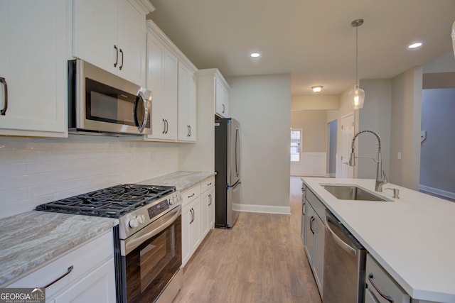 kitchen with light wood-type flooring, appliances with stainless steel finishes, decorative light fixtures, and white cabinets