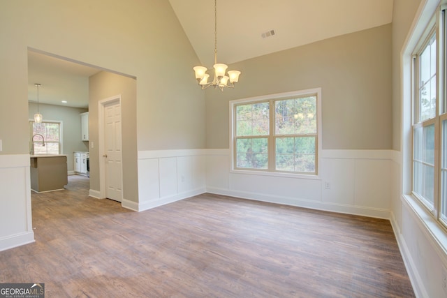 empty room featuring wood-type flooring, an inviting chandelier, and high vaulted ceiling