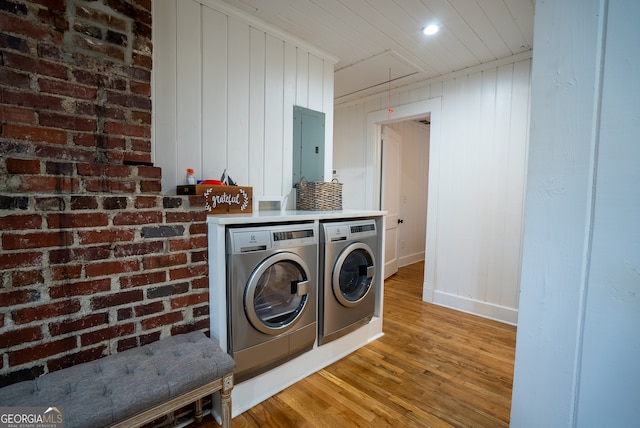 laundry room featuring brick wall, electric panel, washing machine and clothes dryer, wooden walls, and light wood-type flooring