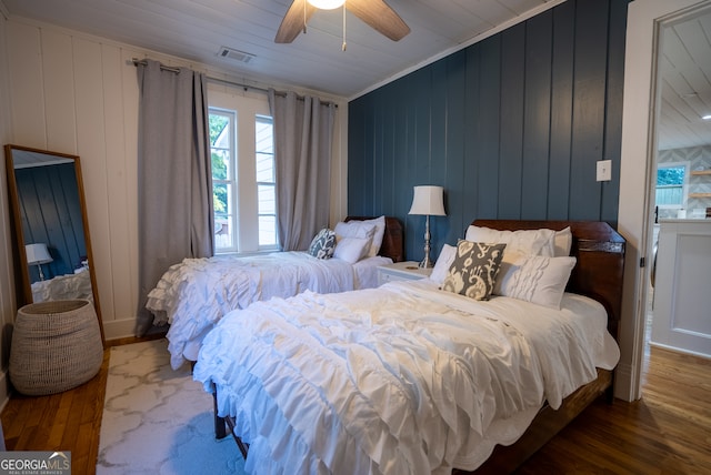 bedroom with ornamental molding, wooden walls, hardwood / wood-style flooring, and ceiling fan