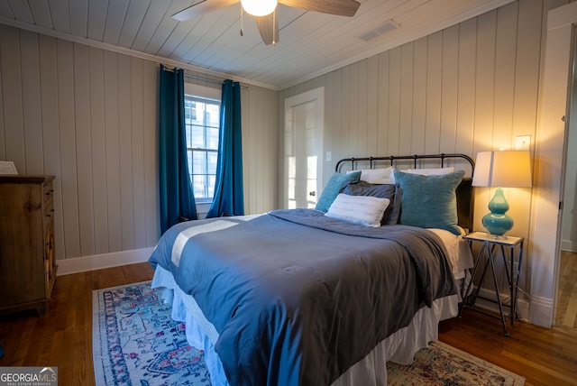 bedroom with ceiling fan, wooden walls, dark hardwood / wood-style flooring, and crown molding