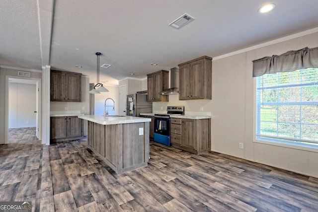 kitchen with pendant lighting, sink, stainless steel appliances, an island with sink, and wall chimney exhaust hood