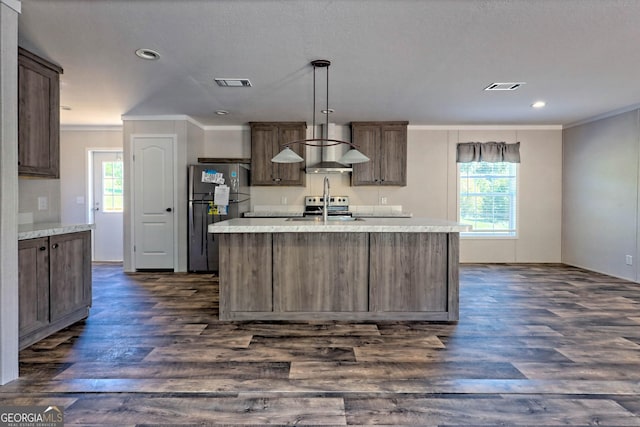 kitchen with dark wood-type flooring, appliances with stainless steel finishes, decorative light fixtures, and an island with sink