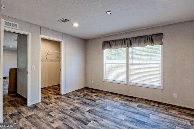 unfurnished bedroom with a walk in closet, dark hardwood / wood-style flooring, a closet, and a textured ceiling