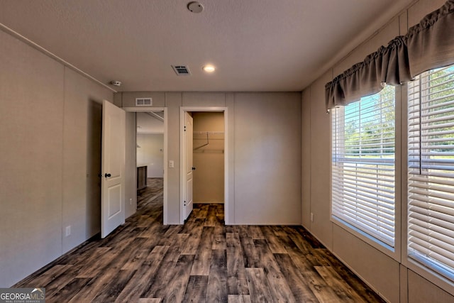 unfurnished bedroom with a spacious closet, dark wood-type flooring, a closet, and a textured ceiling