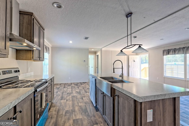 kitchen with sink, an island with sink, pendant lighting, stainless steel appliances, and wall chimney range hood