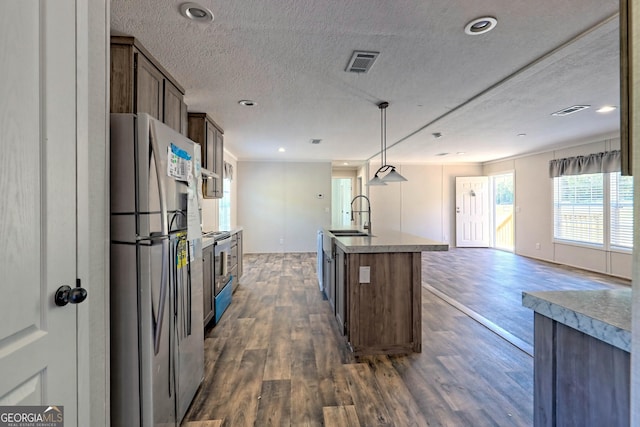 kitchen featuring sink, decorative light fixtures, appliances with stainless steel finishes, dark hardwood / wood-style flooring, and an island with sink