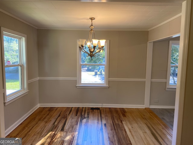 unfurnished dining area featuring hardwood / wood-style flooring, crown molding, and a notable chandelier