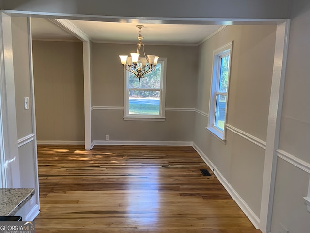 unfurnished dining area with dark wood-type flooring, crown molding, and a notable chandelier