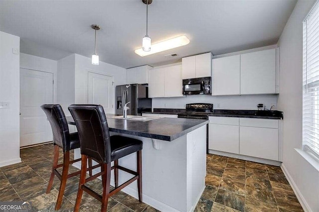 kitchen featuring white cabinetry, a breakfast bar, black appliances, hanging light fixtures, and a kitchen island with sink