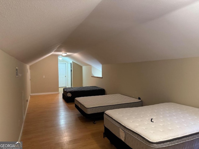 bedroom with hardwood / wood-style flooring, a textured ceiling, and vaulted ceiling