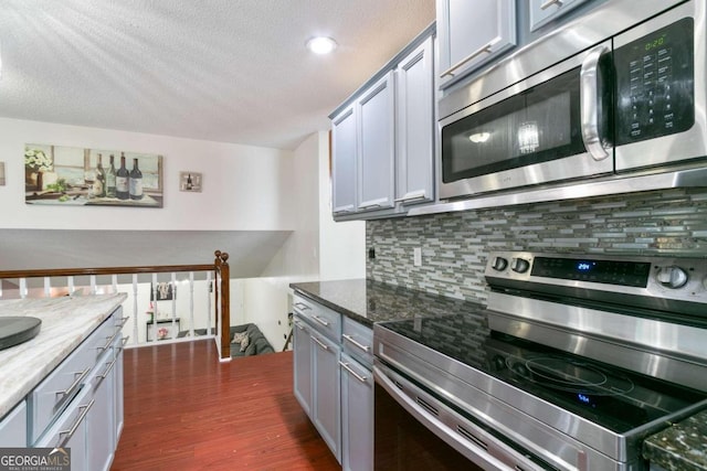 kitchen featuring stainless steel appliances, dark stone countertops, dark hardwood / wood-style flooring, gray cabinets, and decorative backsplash