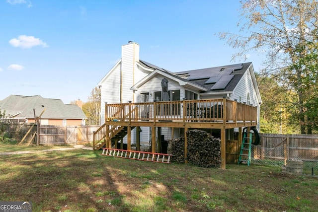 rear view of house featuring a deck, solar panels, and a yard