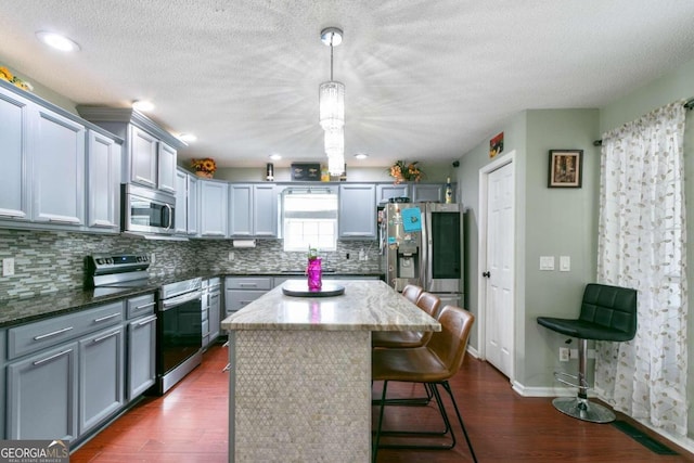 kitchen with pendant lighting, appliances with stainless steel finishes, a kitchen island, and dark hardwood / wood-style flooring