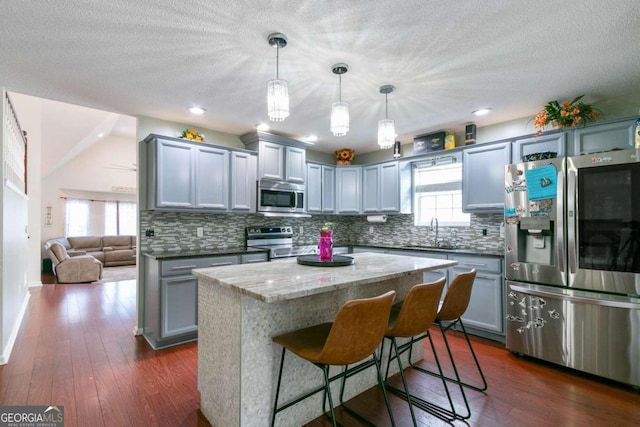 kitchen with stainless steel appliances, dark hardwood / wood-style floors, hanging light fixtures, sink, and a center island