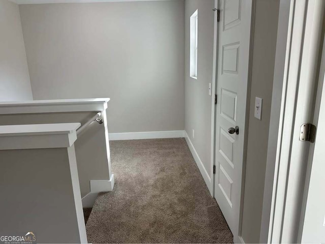 hall with carpet, baseboards, and an upstairs landing