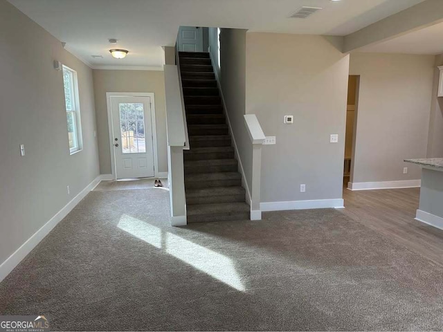 carpeted foyer featuring baseboards, stairs, visible vents, and ornamental molding