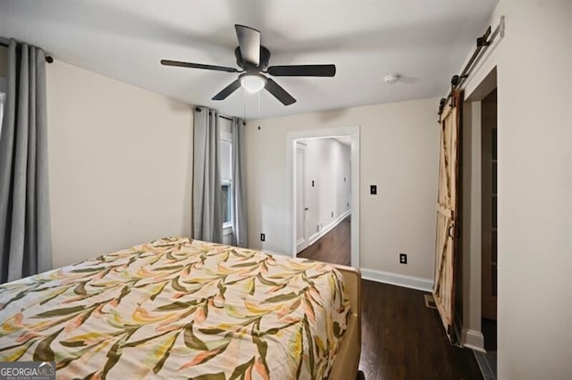 unfurnished bedroom with dark hardwood / wood-style flooring, a barn door, and ceiling fan