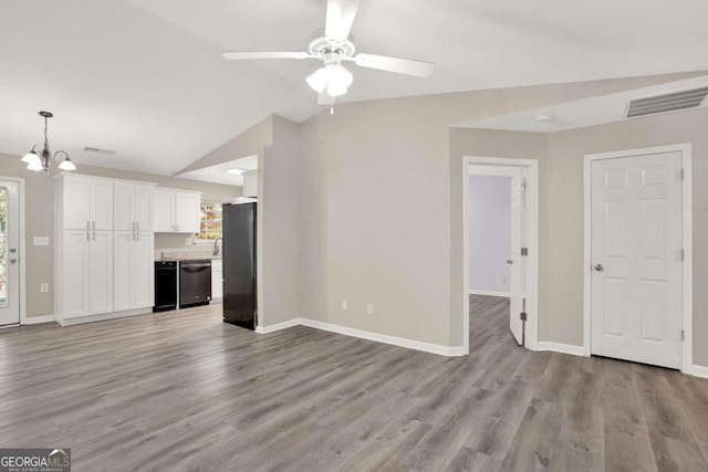 unfurnished living room featuring a wealth of natural light, light hardwood / wood-style floors, vaulted ceiling, and ceiling fan with notable chandelier