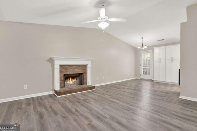 unfurnished living room featuring a brick fireplace, hardwood / wood-style floors, ceiling fan with notable chandelier, and vaulted ceiling