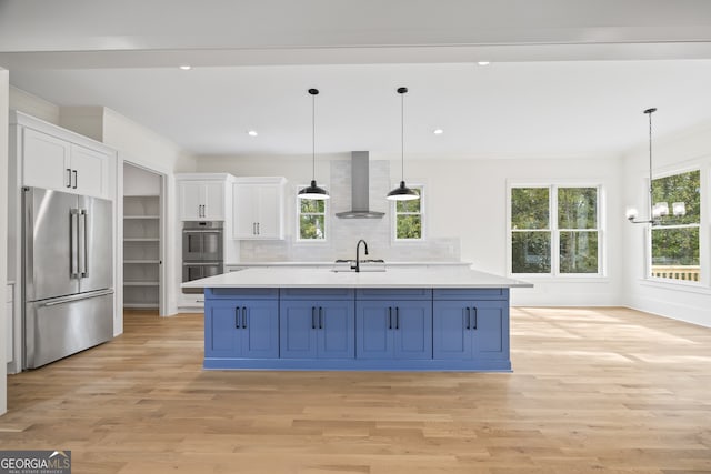 kitchen featuring stainless steel appliances, plenty of natural light, blue cabinets, white cabinets, and wall chimney range hood