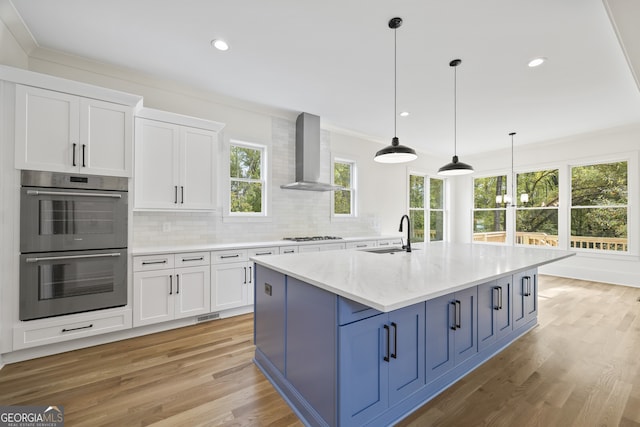 kitchen with light hardwood / wood-style floors, stainless steel appliances, sink, wall chimney range hood, and white cabinetry