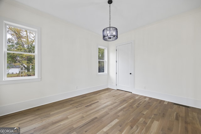 unfurnished dining area featuring wood-type flooring, a chandelier, and ornamental molding