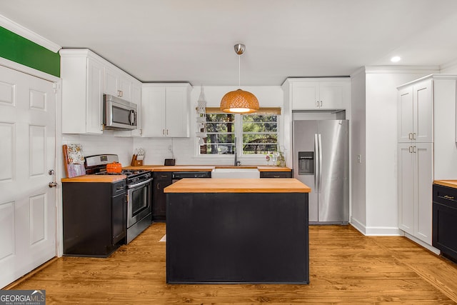 kitchen with appliances with stainless steel finishes, light hardwood / wood-style flooring, a center island, butcher block countertops, and hanging light fixtures