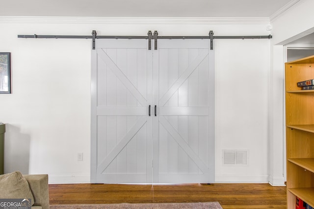 interior space with a barn door, wood-type flooring, and ornamental molding