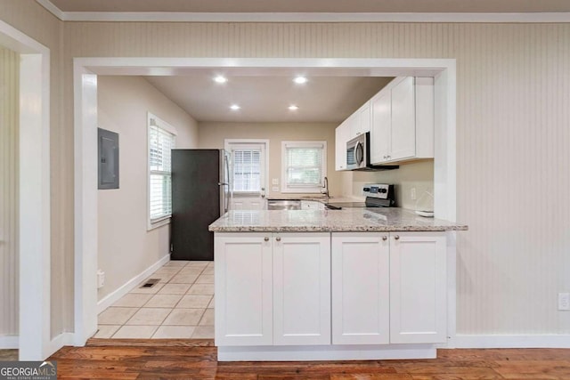 kitchen with white cabinets, stainless steel appliances, light hardwood / wood-style floors, and light stone countertops