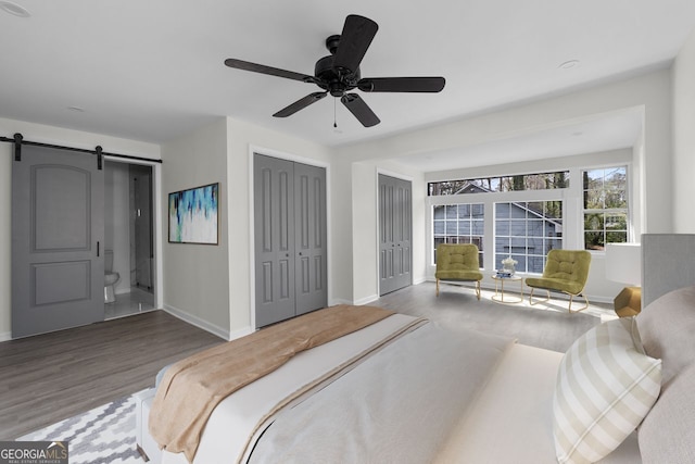 bedroom with a barn door, hardwood / wood-style flooring, ceiling fan, and ensuite bathroom