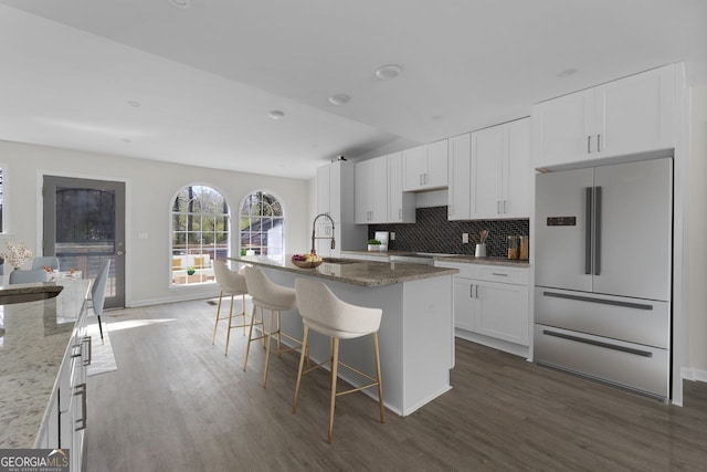 kitchen featuring white cabinetry, light stone counters, high end white fridge, dark hardwood / wood-style floors, and an island with sink