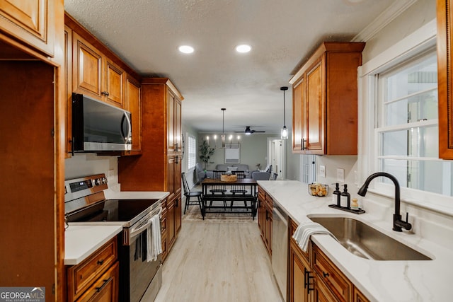 kitchen featuring stainless steel appliances, hanging light fixtures, light stone countertops, a textured ceiling, and sink