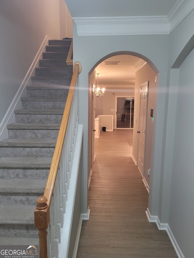 stairway with a chandelier, hardwood / wood-style floors, and crown molding