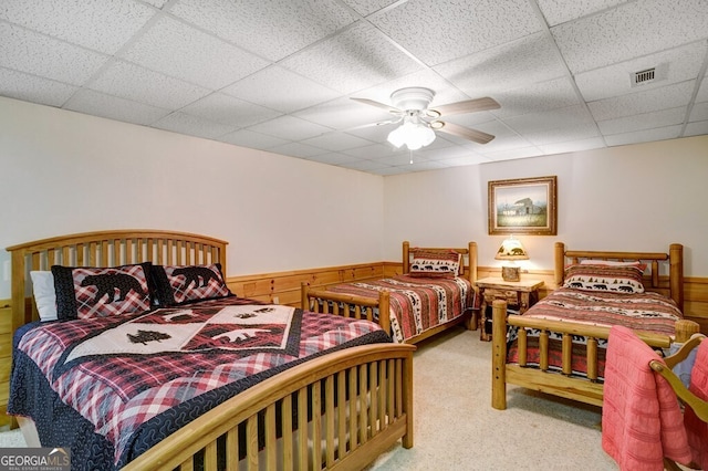 carpeted bedroom with wood walls, ceiling fan, and a paneled ceiling