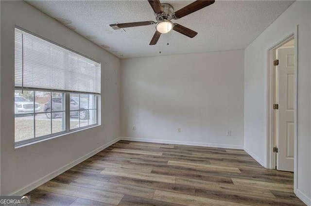 empty room featuring a wealth of natural light, a textured ceiling, and hardwood / wood-style flooring