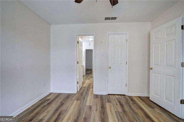 unfurnished bedroom featuring ceiling fan, a textured ceiling, and dark hardwood / wood-style flooring