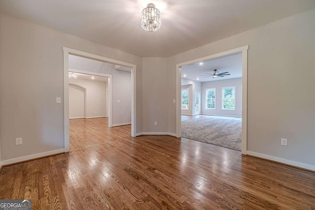 empty room featuring ceiling fan with notable chandelier and hardwood / wood-style flooring