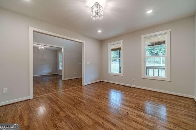 empty room with wood-type flooring and a chandelier