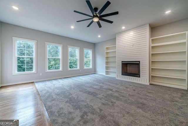 unfurnished living room featuring hardwood / wood-style flooring, ceiling fan, a large fireplace, and built in shelves