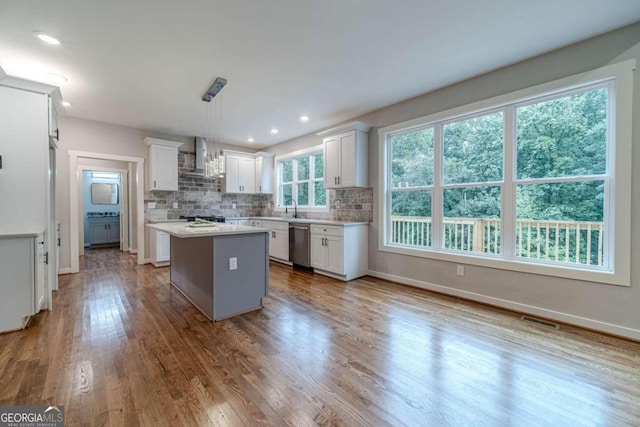 kitchen with white cabinets, hanging light fixtures, stainless steel dishwasher, a kitchen island, and light hardwood / wood-style flooring