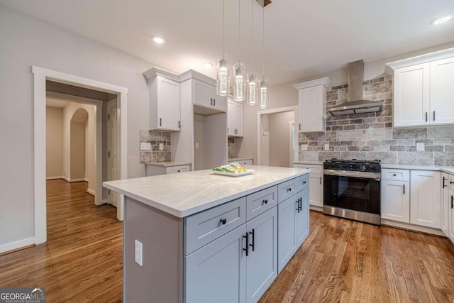 kitchen with white cabinets, wood-type flooring, wall chimney range hood, and stainless steel gas range oven