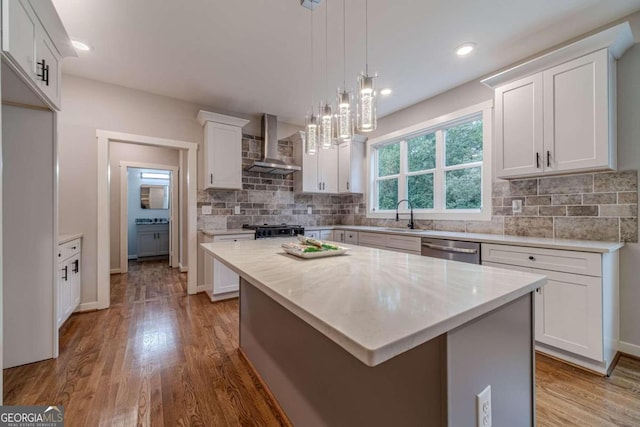 kitchen with wall chimney range hood, white cabinetry, and a kitchen island