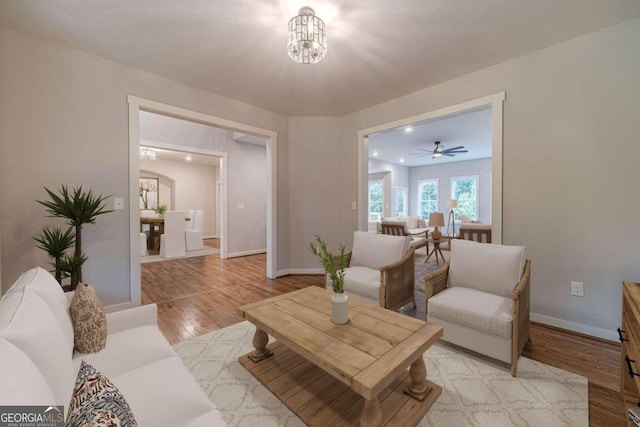 living room with light wood-type flooring and ceiling fan with notable chandelier