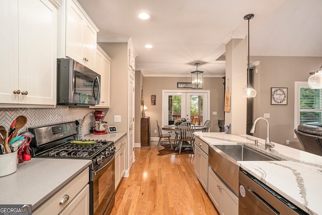 kitchen featuring white cabinets, stainless steel appliances, hanging light fixtures, and light hardwood / wood-style flooring